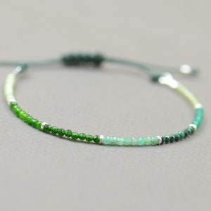 Puede incluir: Un brazalete de cuentas verdes, blancas y plateadas con cierre de nudo deslizante.