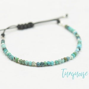 May include: A turquoise beaded bracelet with a black cord and silver accents. The bracelet is adjustable and has a sliding knot.