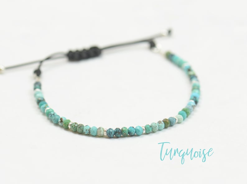 May include: A turquoise beaded bracelet with a black cord and silver accents. The bracelet is adjustable and has a sliding knot.