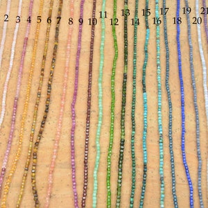 May include: A selection of 23 strands of beads, each strand is a different color and material. The beads are all small and square shaped. The strands are numbered 1 through 23.