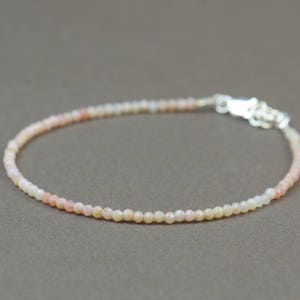 May include: A delicate bracelet made of small, round, white and pink opal beads. The bracelet has a silver clasp.