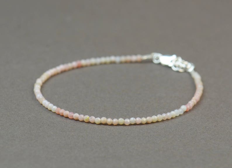 May include: A delicate bracelet made of small, round, white and pink opal beads. The bracelet has a silver clasp.