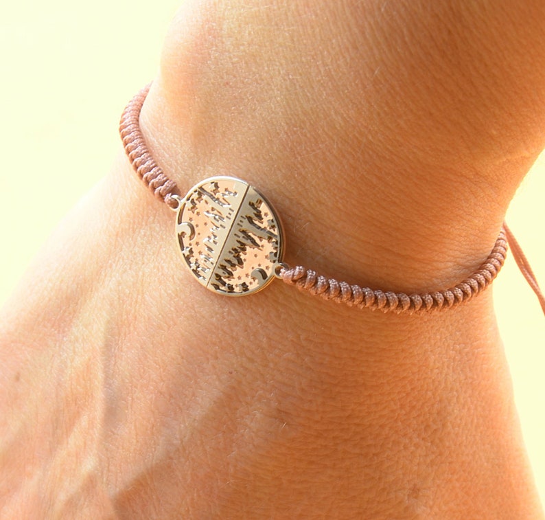 May include: A brown cord bracelet with a round metal charm featuring a tree design.