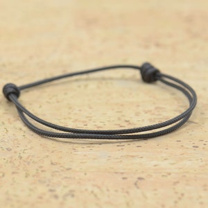 Könnte beinhalten: Ein einfaches, verstellbares Armband aus schwarzem Kordel.