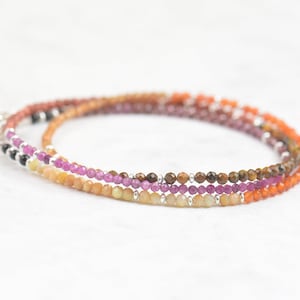May include: A multi-strand bracelet with small, round beads in shades of orange, yellow, pink, and brown. The bracelet is made with natural gemstones and silver.