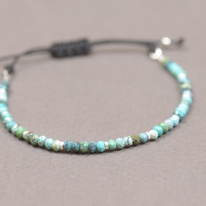 May include: A turquoise and green gemstone beaded bracelet with a black cord and silver toggle clasp.