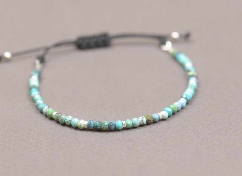 May include: A turquoise and green gemstone beaded bracelet with a black cord and silver toggle clasp.