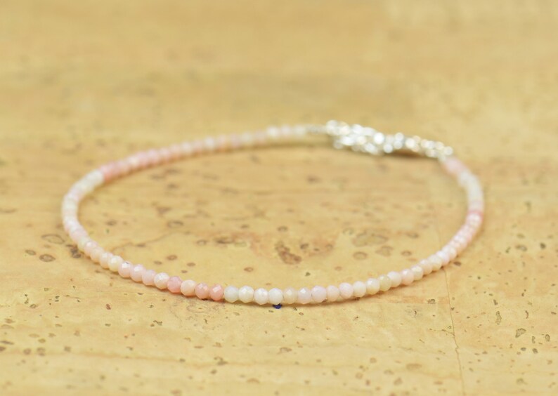 May include: A delicate bracelet made of small, round, pink and white opal beads. The bracelet is strung on a silver chain.