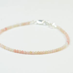 May include: A delicate bracelet made with small, round, pink and white opal beads. The bracelet has a silver clasp.