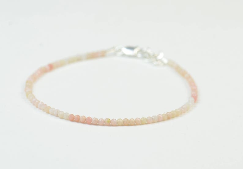 May include: A delicate bracelet made with small, round, pink and white opal beads. The bracelet has a silver clasp.