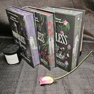 May include: A set of four hardcover books with black covers and floral designs. The titles of the books are "Powerless", "Less", "Less" and "Betrayed Each Other". The books are by author Victoria Aveyard.