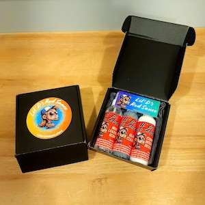 May include: A black box with the Lil' D's Rod Sauce logo and a cartoon character. Inside the box are three bottles of car care products: New Leather Scent, Glass Cleaner, and Ceramic Interior Detailer. The bottles are labeled with the Lil' D's Rod Sauce logo.