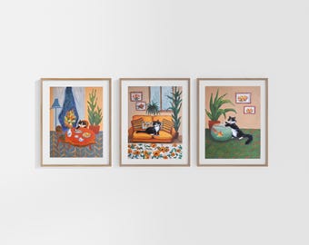 May include: Three framed illustrations of cats in a home setting. The first shows a black and white cat sitting at a table with a cup of tea. The second shows a black and white cat lounging on a yellow couch. The third shows a black and white cat reaching into a fishbowl.