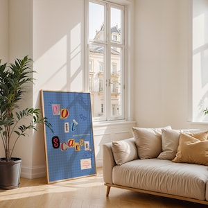 Può includere: Un poster incorniciato con le parole "Do it scared" in lettere colorate in stile ritagliato. Il poster è appoggiato a un muro accanto a una pianta in vaso e a un divano beige con cuscini. La stanza ha grandi finestre.