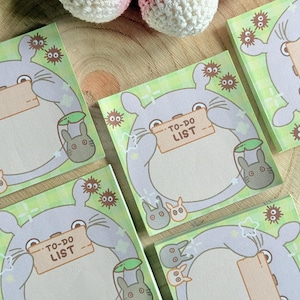 Peut inclure: Bloc-notes carrés avec un personnage de dessin animé tenant une pancarte avec l'inscription "TO-DO LIST". Les blocs-notes ont un fond à carreaux vert et blanc avec des éléments de dessins animés. Les blocs-notes sont conçus pour écrire des notes.