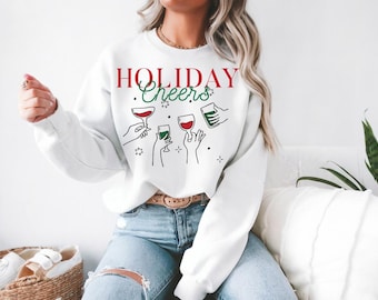 May include: White sweatshirt with a red and green graphic that says "HOLIDAY Cheers" with a design of four hands holding glasses of wine and a beer.