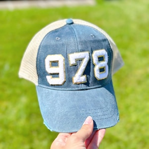 May include: A blue and white trucker hat with the number "978" in white with gold trim on the front.