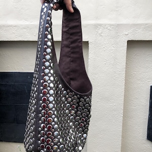 Può includere: Una borsa tote in pelle marrone con borchie argentate. La borsa ha un'unica tracolla e un'ampia apertura.
