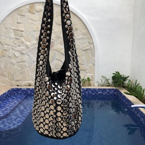 Peut inclure: Un sac à main en cuir noir avec des clous argentés. Le sac a une seule bandoulière et est suspendu au bord d'une piscine.