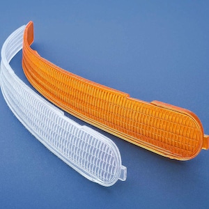 May include: Two curved automotive indicator lenses. One is clear, the other is amber. Both have a textured, ridged surface. The lenses are set against a solid blue background.