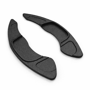 Puede incluir: Dos levas de cambio negras mate, curvas y ergonómicas, se muestran sobre un fondo blanco. Las levas tienen una superficie texturizada y están diseñadas para uso automotriz. El diseño sugiere un enfoque en el rendimiento y la estética.