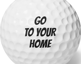 May include: White golf ball with a dimpled surface. The ball has the phrase "GO TO YOUR HOME" printed in bold black letters. The golf ball is designed for recreational use.