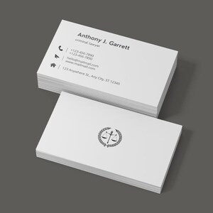 Può includere: Un mazzo di biglietti da visita bianchi con un logo in bianco e nero di una bilancia della giustizia con una corona di alloro. Il testo sulla carta recita "Anthony J. Garrett, avvocato penalista, +123-456-7890, +123-456-7890, 123 Anywhere St. Any Cty, ST 12345".