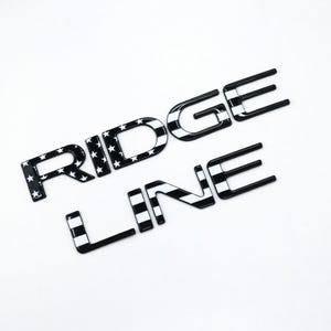 以下が含まれることがあります： 白黒の「RIDGE LINE」エンブレム。 「RIDGE」の文字は白い星が入った黒い背景で、「LINE」の文字は白と黒のストライプのデザインです。 文字は光沢があり、耐久性のある素材で作られているようです。
