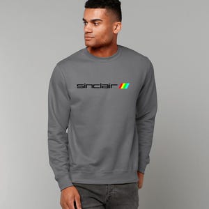 Peut inclure: Un sweat-shirt gris anthracite avec un logo Sinclair noir et un motif de rayures arc-en-ciel.