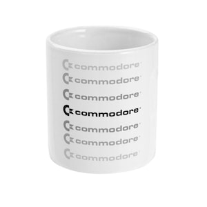 Peut inclure: Une tasse en céramique blanche avec le mot "commodore" répété en lettres noires et grises.