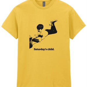May include: Yellow t-shirt with a black and white image of a child using a computer with the text "Saturday's child."
