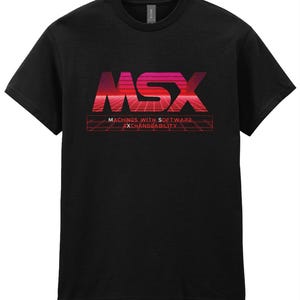 Könnte beinhalten: Schwarzes T-Shirt mit dem Wort "MSX" in einem Retro-Design mit rotem und pinkfarbenem Farbverlauf. Darunter steht in Rot "MACHINES WITH SOFTWARE EXCHANGEABILITY". Das Design hat ein gitterartiges Muster.
