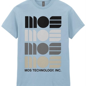 Puede incluir: Una camiseta azul claro con un diseño gráfico de la palabra "MOS" repetida cuatro veces en diferentes tonos de gris. El texto "MOS TECHNOLOGY, INC." está impreso debajo del gráfico.