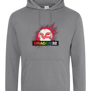 May include: A grey hoodie featuring a red, white and blue Dragon 32 logo with a rainbow paint splatter effect. The logo is enclosed in a white circle with a red background. The text "Dragon 32" is below the logo in black with a rainbow stripe above it.