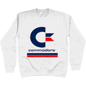 Puede incluir: Sudadera blanca de manga larga con un logotipo de Commodore azul y rojo y la palabra "commodore" en letras azules.