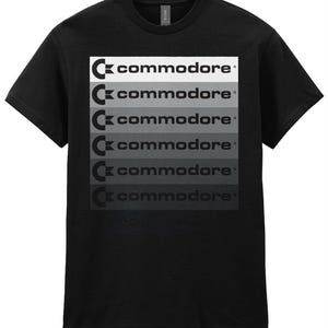 Può includere: Maglietta nera con un design sfumato e stratificato del logo Commodore e la parola "commodore" ripetuta sei volte.