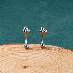 May include: Two silver barbell body jewelry pieces with three small balls on each end.