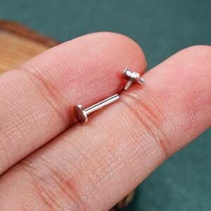 May include: A pair of silver body jewelry pieces. One piece is a flat disc with a post, the other is a star-shaped top with a screw-on post.