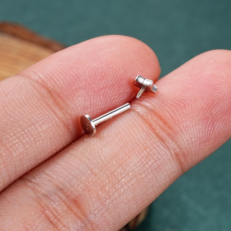May include: A pair of silver body jewelry pieces. One piece is a flat disc with a post, the other is a star-shaped top with a screw-on post.