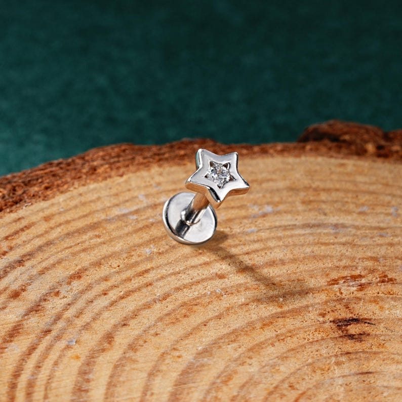 May include: A silver star-shaped stud earring with a clear gemstone in the center. The earring is on a wooden surface.