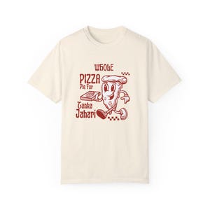 May include: A beige t-shirt with a red graphic of a cartoon pizza slice holding a pizza box. The text on the shirt reads "Whole Pizza Pie For Tanka Jahari".