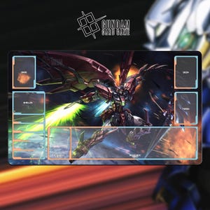 May include: A rectangular Gundam Card Game playmat featuring a detailed illustration of a mecha robot with a green energy beam. The mat has designated zones for cards, with text labels like "Deck" and "Trash". The Gundam Card Game logo is at the top.
