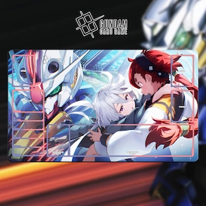 Pode incluir: Tapete de jogo Gundam Card Game retangular com ilustração em estilo anime. O design apresenta um robô Gundam branco e azul e dois personagens de anime se abraçando. O tapete de jogo tem zonas designadas para cartas, com o logotipo Gundam Card Game no topo.