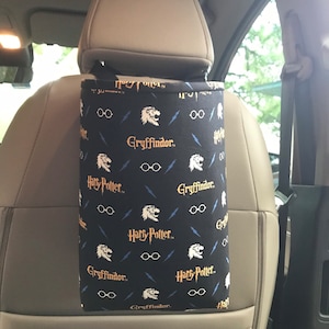 May include: Black car seat back organizer with a Harry Potter themed fabric. The fabric features a repeating pattern of Gryffindor, Harry Potter, lightning bolts, and glasses.