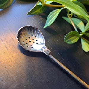Antique  zilverplated spoon in the shape of a shell, attached to a long handle.