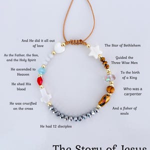 May include: A bracelet with a brown cord and gold-coloured beads. The bracelet features white heart and star-shaped beads, and various coloured beads. The text on the image reads "The Story of Jesus."