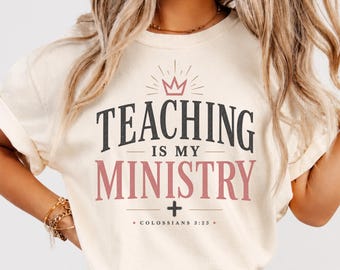 May include: An ivory short-sleeve t-shirt featuring the text "TEACHING IS MY MINISTRY" in dark gray and pink lettering. Above the text is a pink crown icon, and below is a small cross symbol with the scripture reference "COLOSSIANS 3:23".