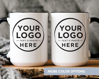May include: Two white ceramic mugs with black handles and rims. Each mug features a circular black graphic containing the text YOUR LOGO, TEXT O PHOTO, and HERE. The design is centered on the front of each mug, showcasing a clean, high-contrast look.