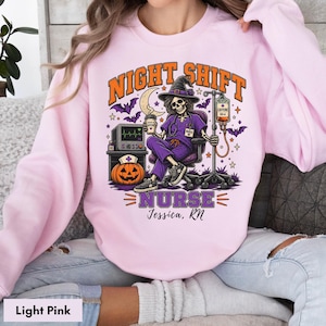 May include: A light pink sweatshirt featuring a graphic of a skeleton nurse in a purple scrub set and witch hat, sitting in a chair with a coffee cup and IV drip. The text reads NIGHT SHIFT NURSE and Jessica, RN, with a pumpkin and monitor.