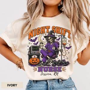 May include: An ivory t-shirt featuring a graphic of a skeleton nurse in a witch hat sitting in a chair, holding a coffee cup. The design includes a pumpkin with a nurse cap, an IV pole, bats, and the text NIGHT SHIFT NURSE Jessica, RN.